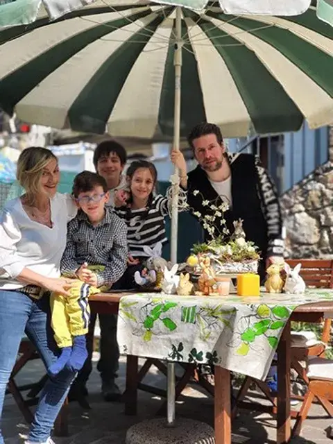 La famiglia dei gestori dell'Hotel Merano a Brenzone sul Garda sorride sotto un ombrellone nel giardino della struttura. 